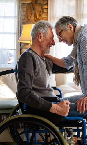 Romantic happy senior couple in love at home. Mature man with disability in wheelchair having fun with wife