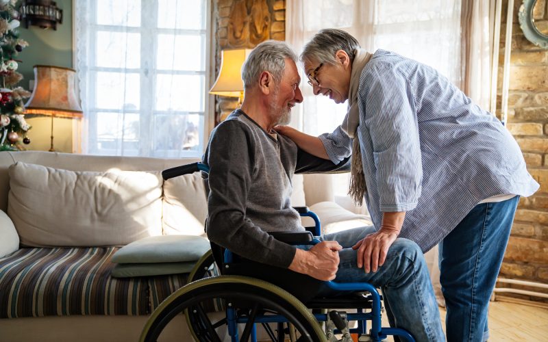 Romantic happy senior couple in love at home. Mature man with disability in wheelchair having fun with wife