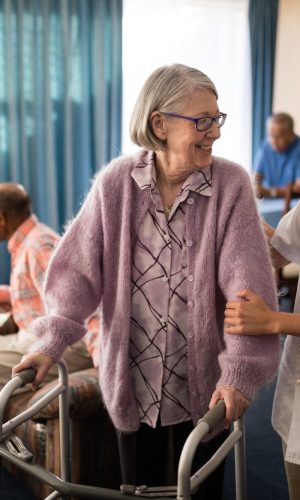 Smiling female doctor looking at senior woman standing with walker in retirement home