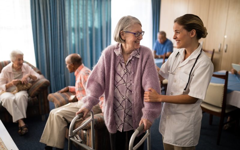 Smiling female doctor looking at senior woman standing with walker in retirement home